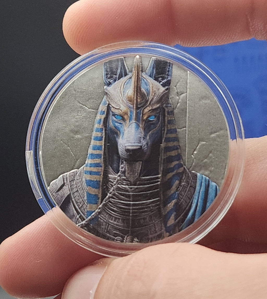 A close-up of a hand holding a round clear plastic capsule containing an illustrated figure with blue, gray, and black details against a dark background.