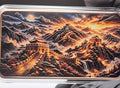 A rectangular metal bar or coin with a detailed landscape print of the Great Wall of China, held by black-gloved hands over a white circular platform against a dark background.