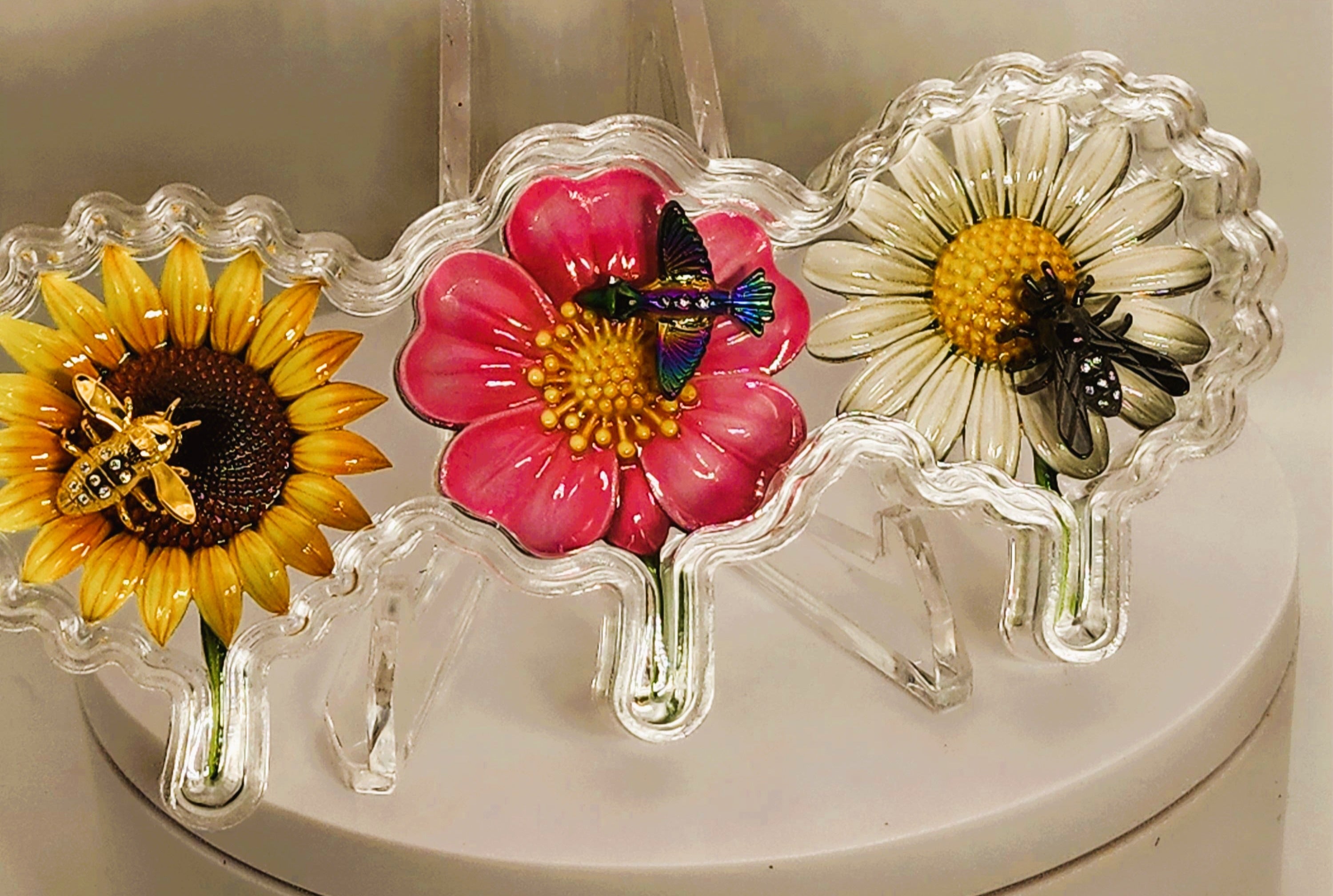 Three decorative flower-shaped glass keepsakes with bees, displayed on a round white box against a beige background.