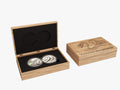 Two silver coins in a wooden box with a snake design on a white background